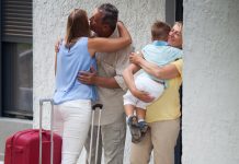 Woman and little son with suitcases arriving. Happy people embracing by the house entrance