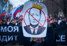man in blue jacket holding white and red bird print banner