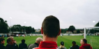 man standing while watching soccer during daytime