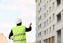 Back view portrait of unrecognizable engineer holding plans standing at construction site outdoors, copy space